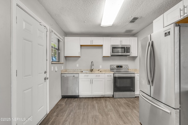 kitchen with sink, a textured ceiling, stainless steel appliances, light hardwood / wood-style floors, and white cabinets