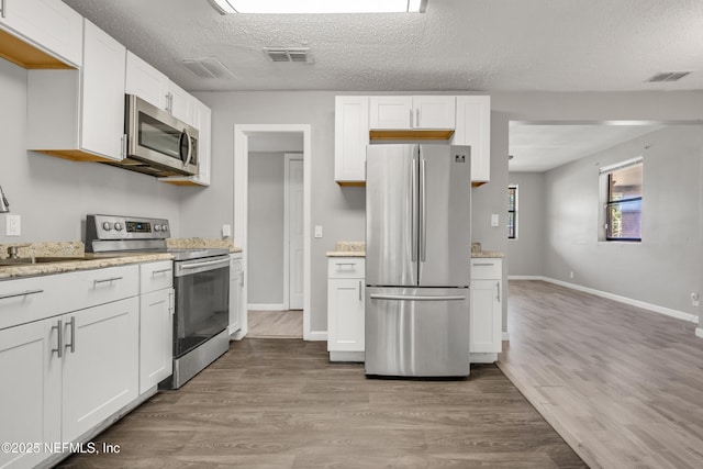 kitchen with wood-type flooring, appliances with stainless steel finishes, white cabinets, and a textured ceiling