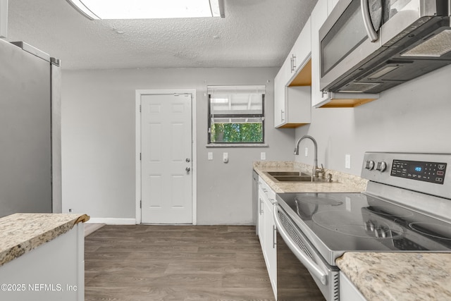 kitchen with sink, appliances with stainless steel finishes, white cabinetry, hardwood / wood-style floors, and a textured ceiling