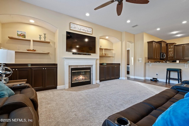 living room featuring ceiling fan, light carpet, a tile fireplace, and built in features