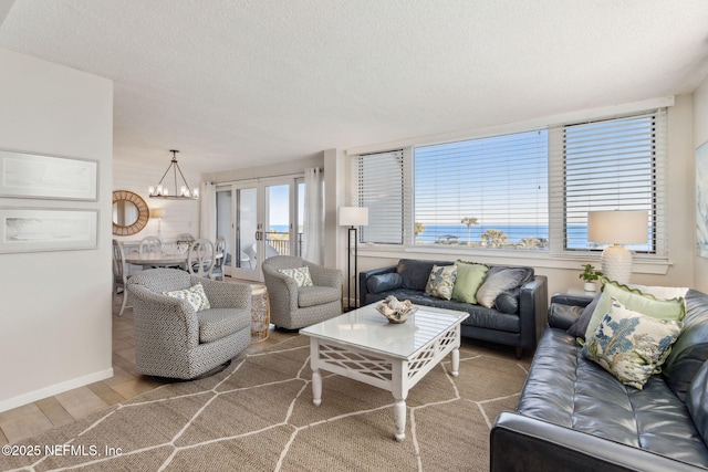 living room with an inviting chandelier, hardwood / wood-style floors, a water view, a textured ceiling, and french doors