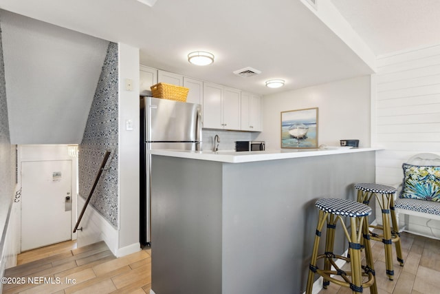 kitchen with white cabinetry, a breakfast bar area, stainless steel fridge, backsplash, and kitchen peninsula