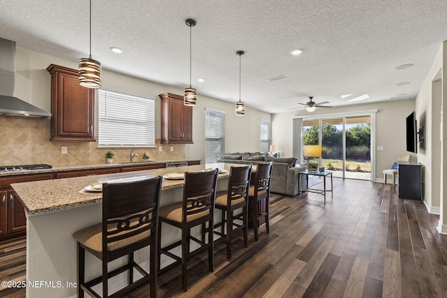 kitchen featuring a center island, wall chimney range hood, a kitchen bar, and decorative light fixtures