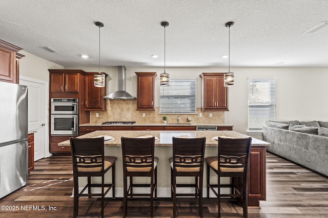 kitchen featuring a breakfast bar area, hanging light fixtures, a center island, stainless steel appliances, and wall chimney exhaust hood