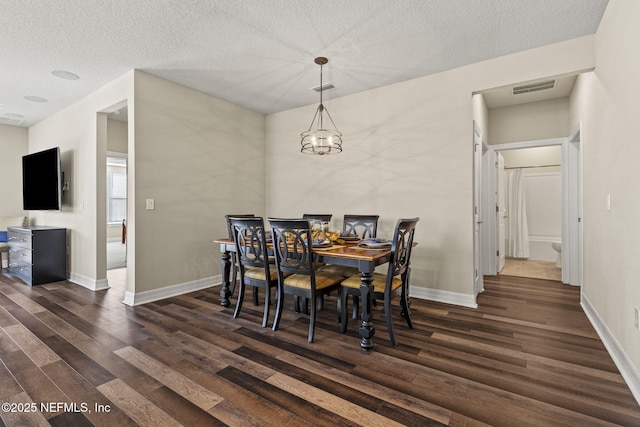 dining area featuring dark wood-type flooring, a textured ceiling, and an inviting chandelier