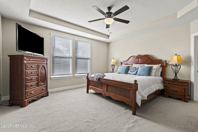 bedroom with light colored carpet, a tray ceiling, and a textured ceiling