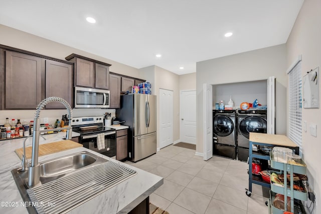 kitchen with sink, appliances with stainless steel finishes, dark brown cabinetry, washing machine and clothes dryer, and light tile patterned flooring