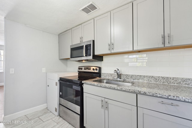 kitchen featuring sink, white cabinetry, appliances with stainless steel finishes, light stone countertops, and decorative backsplash