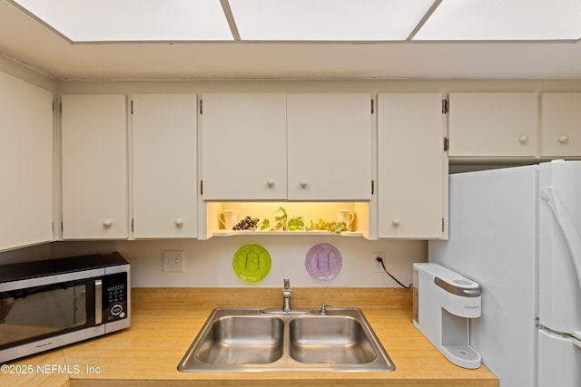 kitchen featuring white refrigerator, white cabinetry, and sink