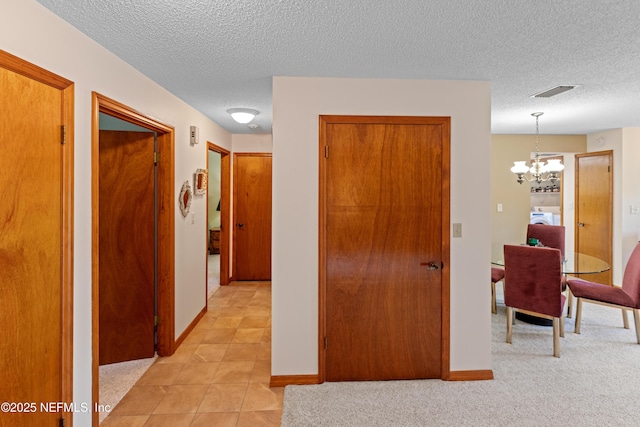 hall with an inviting chandelier, light colored carpet, and a textured ceiling