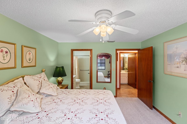 bedroom with ceiling fan, light tile patterned floors, a textured ceiling, and ensuite bath