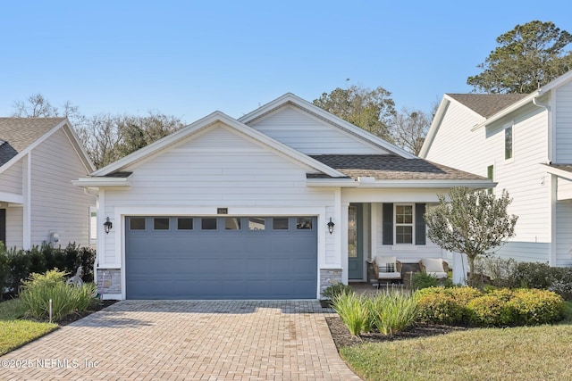 view of front of home with a garage, stone siding, a shingled roof, and decorative driveway