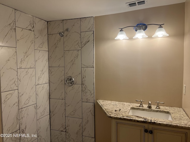 bathroom featuring visible vents, a tile shower, and vanity