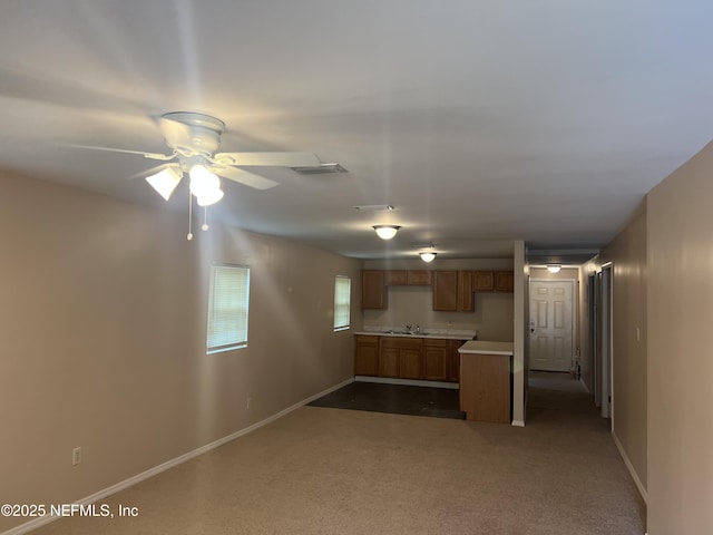 unfurnished living room with ceiling fan, dark colored carpet, a sink, and baseboards