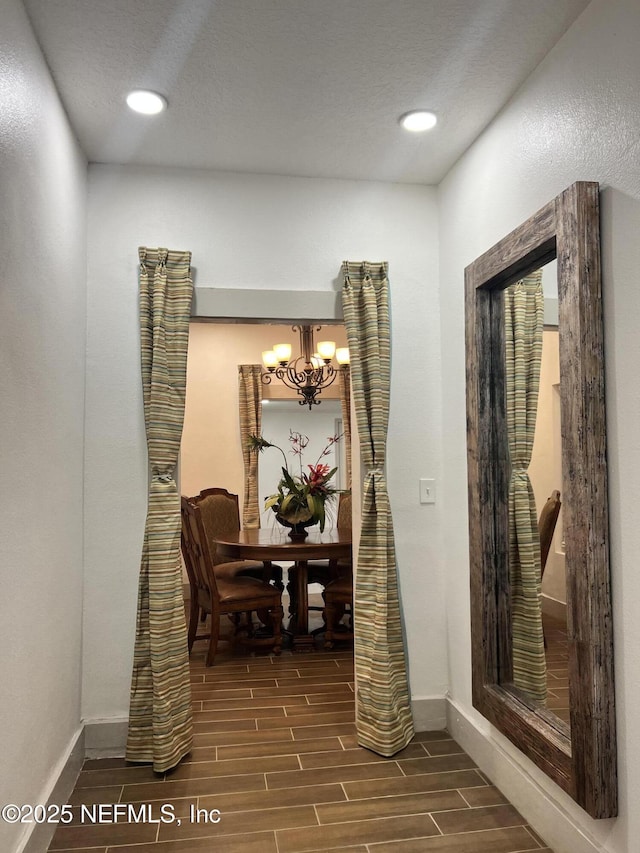 corridor featuring baseboards, wood finish floors, recessed lighting, and an inviting chandelier