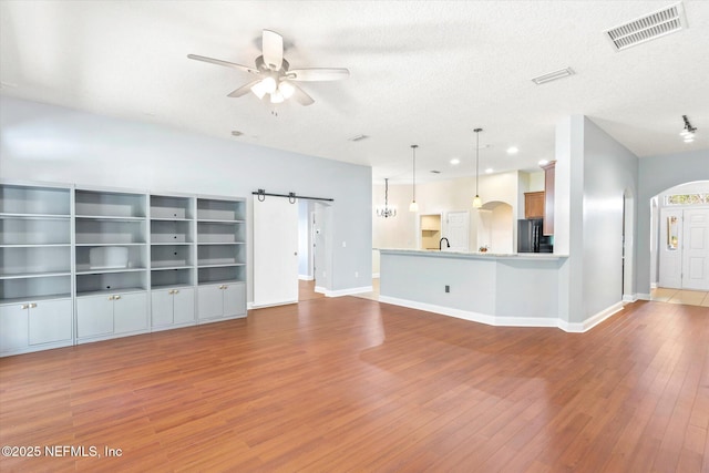 unfurnished living room with a textured ceiling, light hardwood / wood-style flooring, a barn door, and ceiling fan