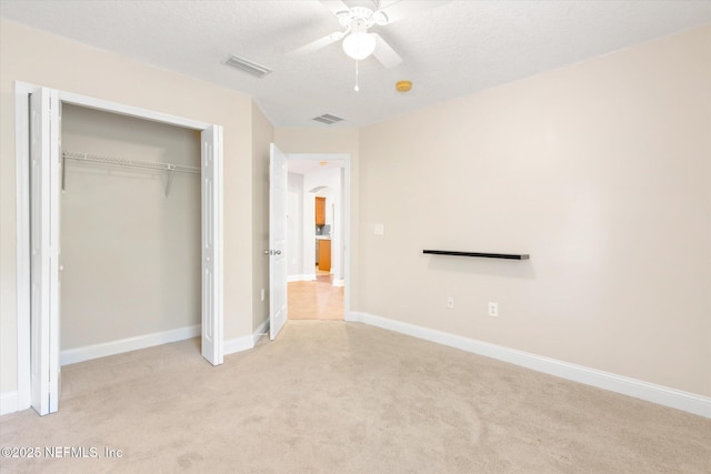 unfurnished bedroom with ceiling fan, light colored carpet, a closet, and a textured ceiling