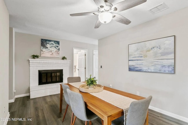 dining area with a brick fireplace, dark hardwood / wood-style floors, and ceiling fan