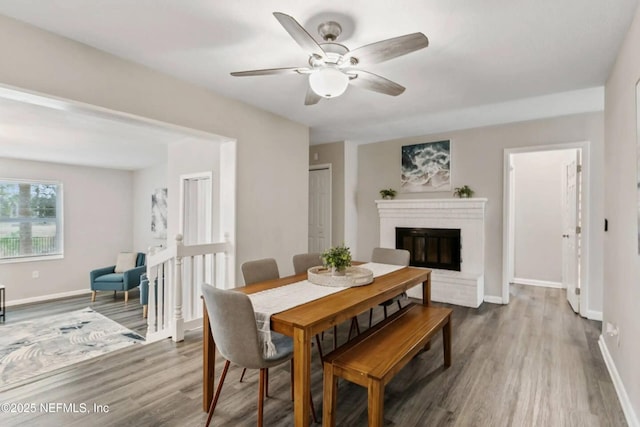 dining area with wood-type flooring, a brick fireplace, and ceiling fan