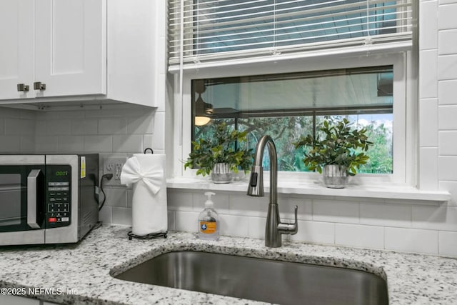 interior details featuring white cabinetry, sink, backsplash, and light stone countertops