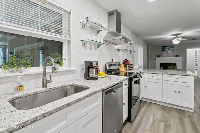 kitchen featuring sink, light stone counters, island range hood, appliances with stainless steel finishes, and white cabinets