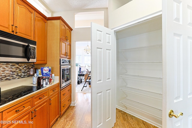 kitchen featuring backsplash, appliances with stainless steel finishes, a textured ceiling, and light wood-type flooring