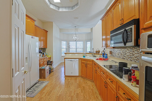 kitchen with sink, decorative light fixtures, light wood-type flooring, kitchen peninsula, and white appliances