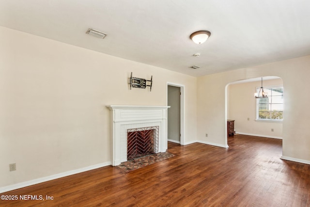 unfurnished living room featuring baseboards, visible vents, arched walkways, wood finished floors, and a brick fireplace