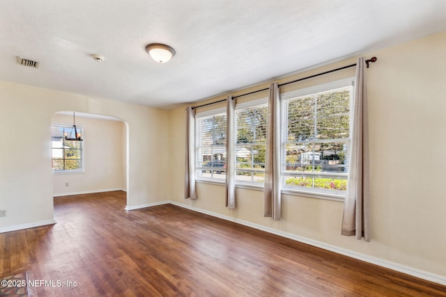 unfurnished room featuring arched walkways, visible vents, an inviting chandelier, wood finished floors, and baseboards