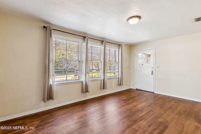 empty room with wood finished floors, visible vents, and baseboards