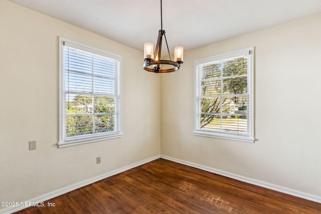 spare room featuring a healthy amount of sunlight, dark wood-style floors, baseboards, and an inviting chandelier