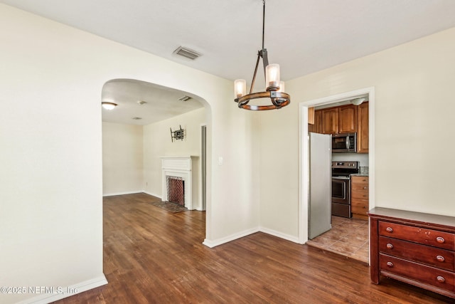 unfurnished dining area featuring a fireplace with flush hearth, arched walkways, visible vents, and dark wood finished floors