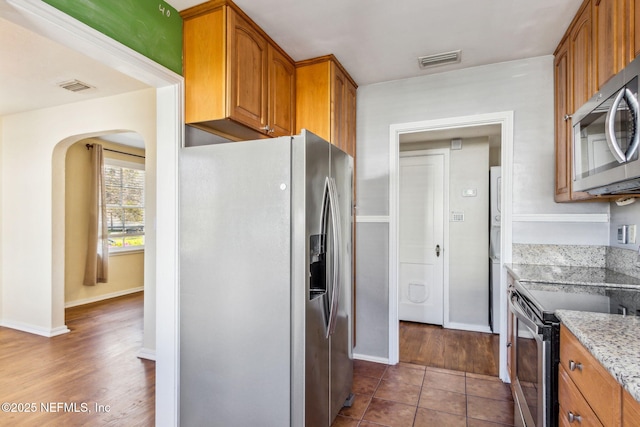 kitchen with light stone counters, appliances with stainless steel finishes, brown cabinetry, and visible vents