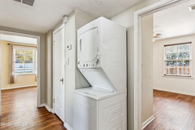 clothes washing area with laundry area, dark wood-type flooring, stacked washing maching and dryer, and visible vents