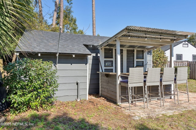 back of property featuring a shingled roof, fence, and outdoor dry bar