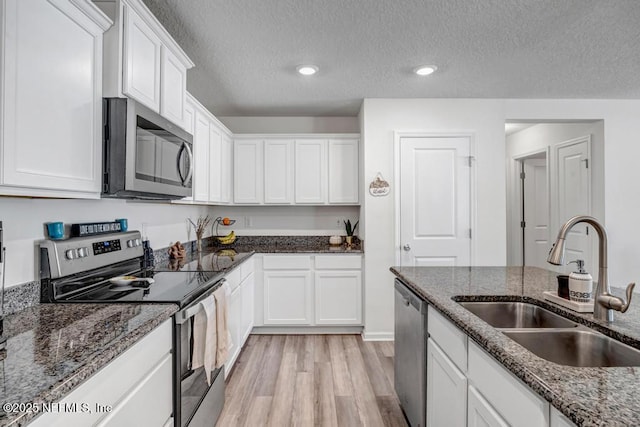 kitchen with stainless steel appliances, white cabinetry, sink, and dark stone countertops