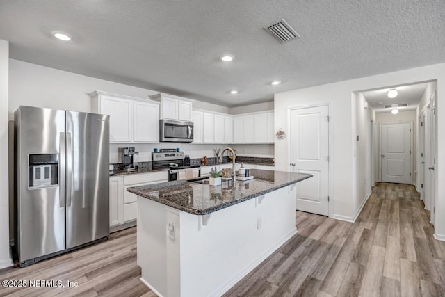 kitchen with sink, appliances with stainless steel finishes, an island with sink, white cabinets, and dark stone counters