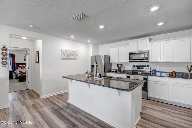 kitchen with white cabinetry, stainless steel appliances, a kitchen breakfast bar, and a center island with sink