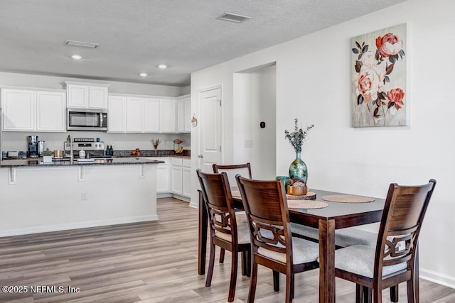 kitchen featuring appliances with stainless steel finishes, white cabinetry, dark stone countertops, light hardwood / wood-style floors, and a textured ceiling