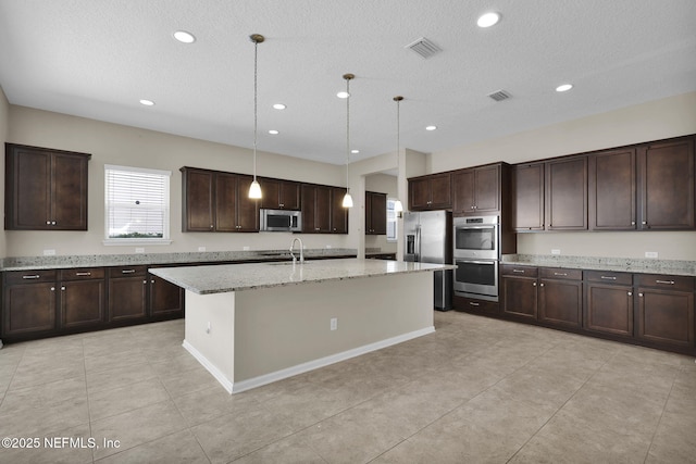 kitchen featuring sink, appliances with stainless steel finishes, dark brown cabinetry, an island with sink, and decorative light fixtures