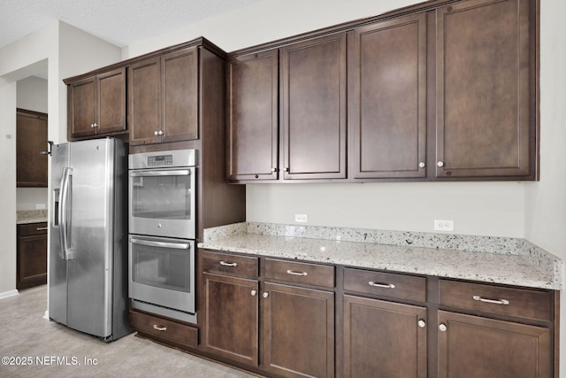 kitchen with light stone countertops, dark brown cabinets, and stainless steel appliances