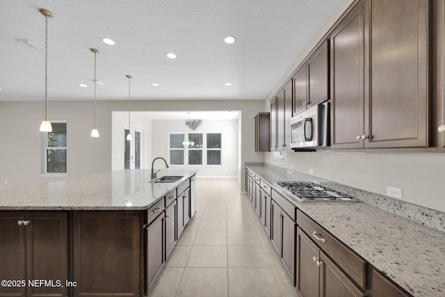 kitchen with sink, hanging light fixtures, a kitchen island with sink, stainless steel appliances, and light stone countertops