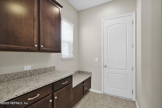 kitchen featuring dark brown cabinets, light tile patterned floors, and light stone counters