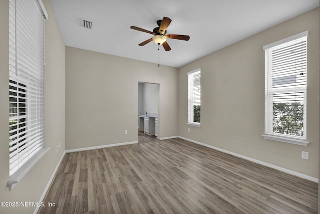 empty room with ceiling fan, a wealth of natural light, and wood-type flooring