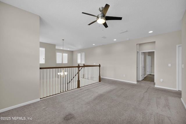 spare room with ceiling fan with notable chandelier, light colored carpet, and a textured ceiling