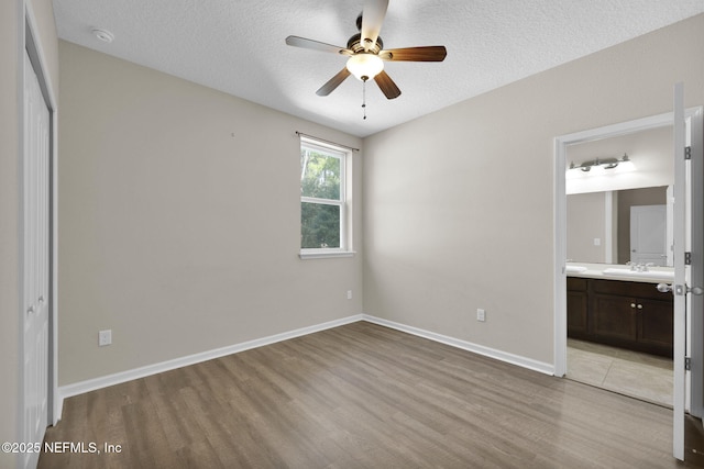 unfurnished bedroom featuring sink, connected bathroom, a textured ceiling, and light hardwood / wood-style floors