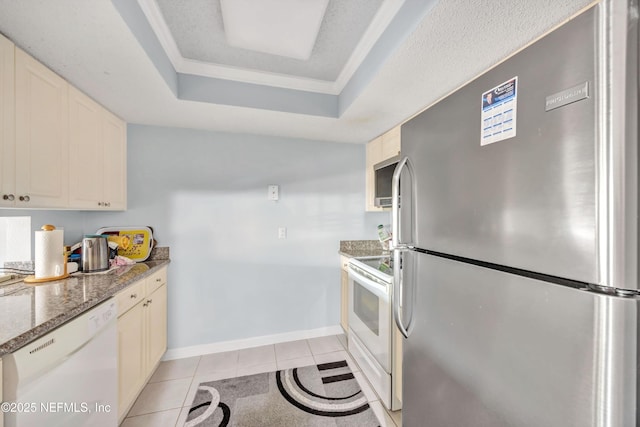 kitchen with light tile patterned flooring, white appliances, a tray ceiling, and dark stone countertops