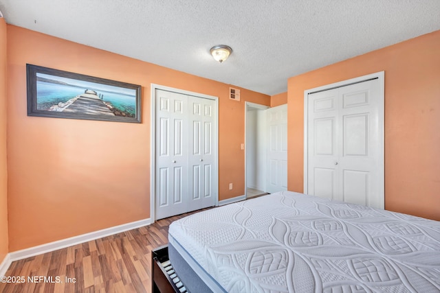 bedroom featuring hardwood / wood-style floors, a textured ceiling, and two closets