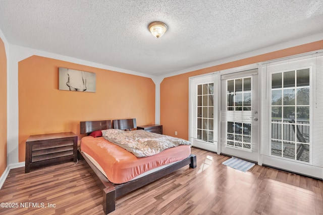 bedroom featuring hardwood / wood-style floors, access to outside, and a textured ceiling