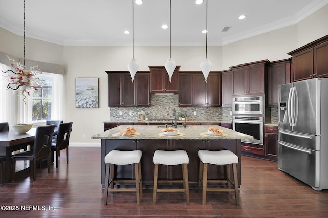 kitchen featuring decorative light fixtures, decorative backsplash, a kitchen island with sink, light stone counters, and stainless steel appliances